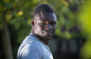 Parkta duran gülümseyen ve memnun genç Afrikalı adamın portresi.