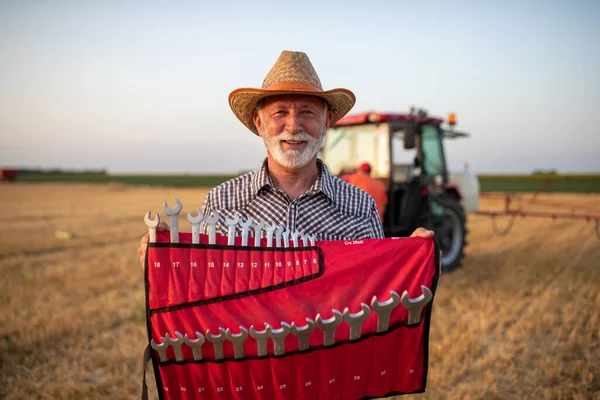 畑のトラクターの前にレンチのセットを保持するシニア農家の肖像画 — ストック写真