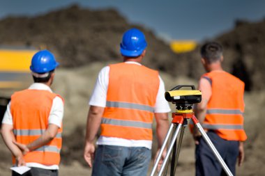 Theodolite and workers at construction site clipart