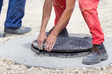 Worker installing cover at manhole clipart