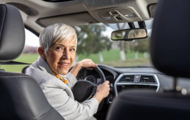 Gülümseyen son sınıf öğrencisi kadın arabada oturuyor ve arkasına bakıyor.  