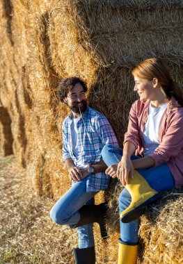 Erkek ve kadın bir saman yığınına yaslanıyor ve oturuyor, tarlada sıkı çalıştıktan sonra dinleniyorlar.