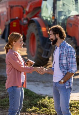 Sığır çiftliğinde tokalaşan iki çiftçi. Güneşli sonbahar gününde arka planda duran besleme karıştırıcılı traktör