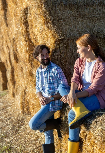 Erkek ve kadın bir saman yığınına yaslanıyor ve oturuyor, tarlada sıkı çalıştıktan sonra dinleniyorlar.