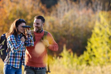 Birkaçı doğayı birlikte tecrübe ederken kuş gözlemciliği, renkli sonbahar yapraklarıyla çevrili, tek eşli dürbün kullanıyor..