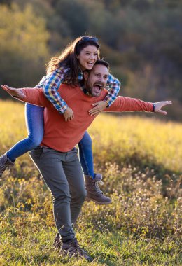 Mutlu bir çift gün boyunca çimenli bir alanda eğleniyor. Adam kadını sırtında taşırken onlar gülüyor ve neşeyle poz veriyor.