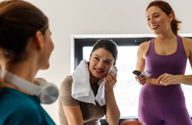 Spor salonunda egzersiz sonrası rahatlama. Üç genç kadın sabah eğitiminden sonra sohbet ediyorlar.