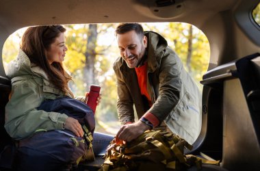 Bir çift, güneşli bir sonbahar gününde, renkli yapraklar ve doğa ile çevrili arabalarının arkasında ekipmanlarını hazırlamaktan zevk alır..