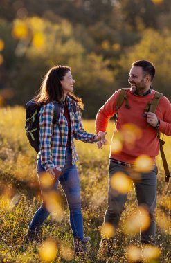 Renkli yapraklar ve altın güneş ışığıyla çevrili güneşli bir sonbahar parkında el ele dolaşırlar. Gülüşleri ve kahkahaları paylaşıyorlar