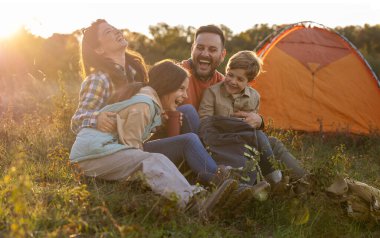 Dört kişilik bir aile bir tarlada bir arada oturur güneş batarken güler ve gülümserler. Kamp çadırlarının yanında keyifli bir anı paylaşıyorlar..