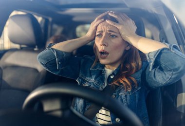 Arabada endişeli bir kadın oturuyor. Başını tutuyor ve dışarıda beklenmedik bir olaya tepki veriyor gibi görünüyor..