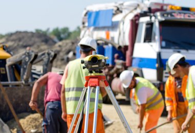 Theodolite and workers at construction site clipart