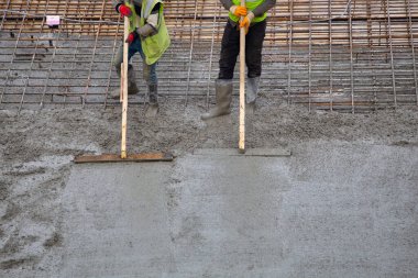 Masons leveling fresh poured concrete at the building site. clipart