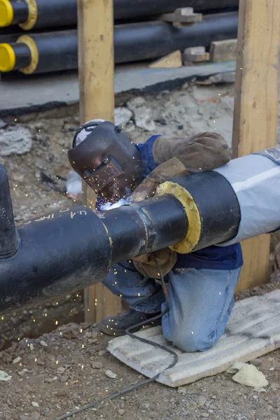 Svetsare svetsning underground stålrör knäböjer på marken 2 — Stockfoto