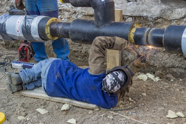 Welder welding underground steel pipe lying on ground — Stock Photo, Image