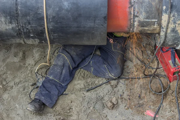 Soldador trabajador moliendo la soldadura en zanja bajo tubería — Foto de Stock