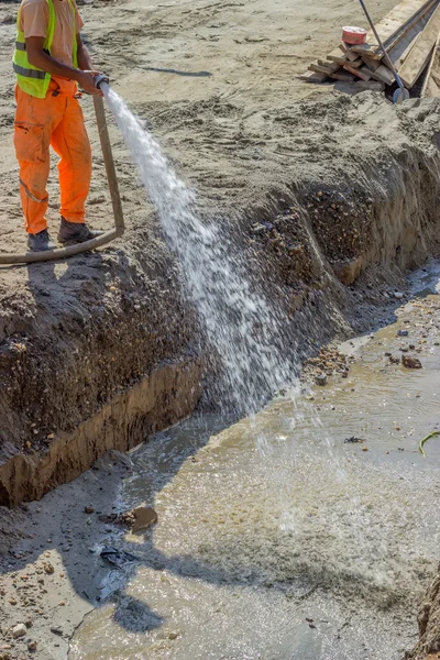 Il lavoratore bagna la superficie di corso di base aggregata schiacciata — Foto Stock