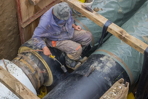 Insulation worker applied tar coating on underground heating pip — Stock Photo, Image