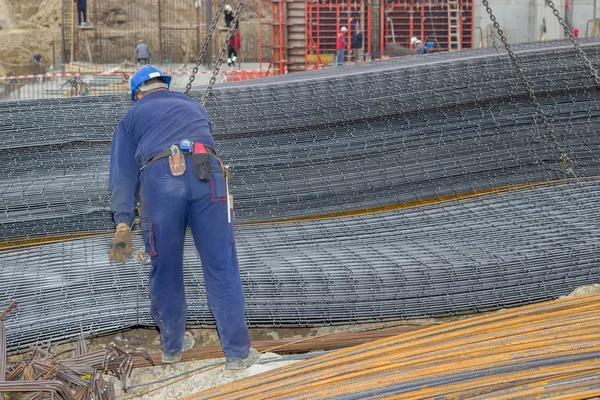 Железный рабочий выгружает арматуру из крана для строительства — стоковое фото
