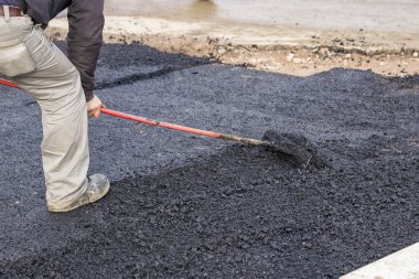 Worker using rake to level asphalt pavement 3 clipart