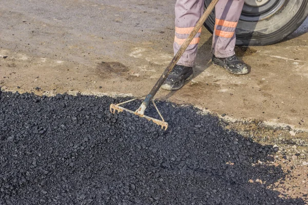 Worker using rake to level asphalt pavement — Stock Photo, Image