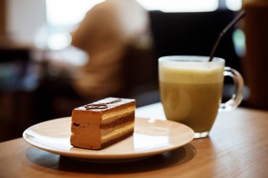 Kahverengi çikolatalı pasta, üzerinde üç tuşlu bir anahtarın müzikal sembolü ve kafedeki masada bir bardakta kahve içeceği var..