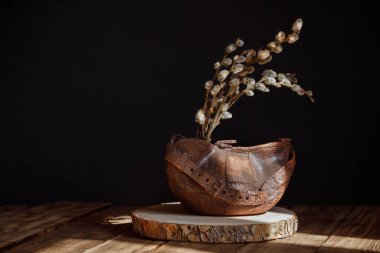 Söğüt dallarıyla yapılmış seramik vazo. Eski tahtalardan yapılmış ahşap bir masanın üzerinde duruyor. Doğal kırsal sabah konsepti. Gösterişsiz ışıklandırma ve asgari sanat tarzında klasik bir hayat..