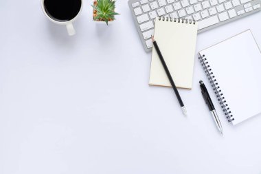 Beyaz ofis masasının üstünde klavye, defter ve kahve fincanı ve diğer ofis malzemeleri. İş ve finans kavramı. Çalışma yeri, boş kopya alanı olan düz uzanma