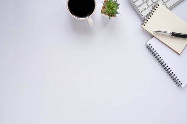 Klavyeli beyaz ofis masası, defter ve kahve fincanı diğer ofis malzemeleriyle dolu. İş ve finans kavramı. İşyeri, boş fotokopi alanı olan düz bir yer. Üst görünüm