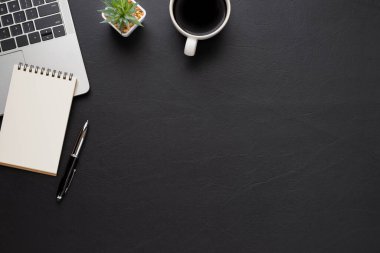 Siyah deri ofis masasının üstünde klavye, not defteri ve ekipman ofis malzemeleriyle dolu kahve fincanı. İş ve finans kavramı. Çalışma yeri, boş kopya alanı olan düz uzanma.