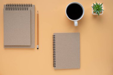 Brown 'ın üst manzarası kapalı sarmal boş kağıt kapaklı defter ve kalem. Kahverengi arka planda bir kahve fincanı var. Model tasarlamak için. Eğitim ve iş konsepti. düz yat