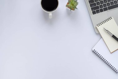 Beyaz ofis masasının üstünde klavye, defter ve kahve fincanı ve diğer ofis malzemeleri. İş ve finans kavramı. Çalışma yeri, boş kopya alanı olan düz uzanma.