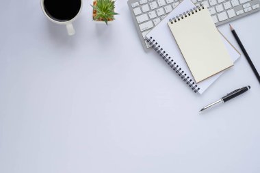Beyaz ofis masasının üstünde klavye, defter ve kahve fincanı ve diğer ofis malzemeleri. İş ve finans kavramı. Çalışma yeri, boş kopya alanı olan düz uzanma.