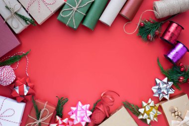 Noel tatili arkaplanının üstündeki en iyi manzara. Kırmızı arka planda köknar dalları, kurdele, fiyonk ve hediye kutusu süslemeleri olan kompozisyon. Kış, Noel, yeni yıl konsepti. Düz yat, boşluğu kopyala.