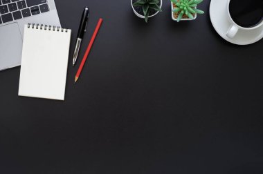 Siyah ofis masasının üstünde dizüstü bilgisayarı ve diğer ofis malzemeleriyle dolu bir not defteri var. İş ve finans kavramı. Çalışma yeri, boş kopya alanı olan düz uzanma.