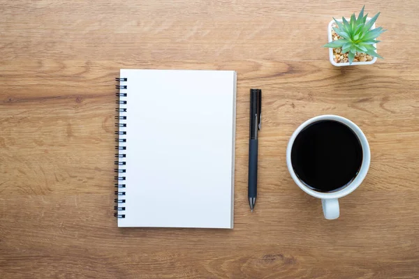 Tahta arka planda boş defter, kalem ve kahvenin üst görüntüsü. Tasarımcı için evde yaratıcı bir iş yeri. Fotokopi alanı olan düz alan, işletme finansmanı veya eğitim kavramı.