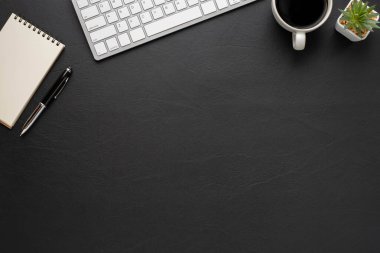 Üzerinde klavye, defter ve kahve fincanı olan siyah deri ofis masası diğer ofis malzemeleriyle dolu. İş ve finans kavramı. Çalışma yeri, boş kopya alanı olan düz uzanma.