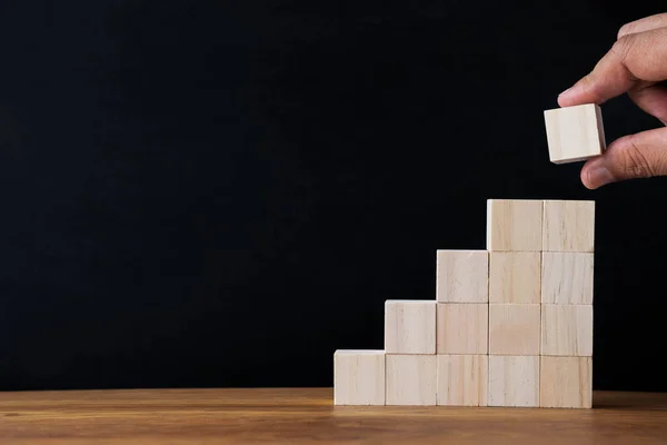 Hand arranging wood blocks stacking as step stair on wooden table background. Business investment and finance accounting concept for growth success process with copy space.