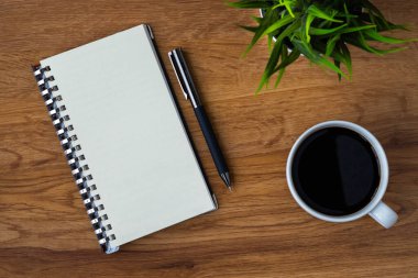 Boş sayfaları olan açık okul defterinin en üst görüntüsü, tahta masa arkaplanına not almak için kahve fincanı ve kalem. Düz yatış, yaratıcı çalışma alanı ofisi. Kopya alanı ile işletme eğitimi kavramı.