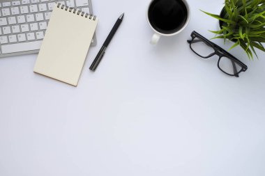 Beyaz ofis masasının üstünde klavye bilgisayarı, not defteri ve kahve fincanı ve diğer ofis malzemeleri. İş ve finans kavramı. Çalışma yeri, boş kopya alanı olan düz uzanma.