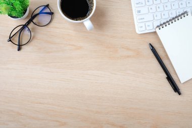 Ahşap ofis masasının üstünde klavye, not defteri ve not defteri olan bir masa. İçinde ekipman ofis malzemeleri olan bir kahve fincanı. İş ve finans kavramı. Çalışma yeri, boş kopya alanı olan düz uzanma.