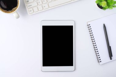 Tabletin üstündeki boş ekranın üst görüntüsü beyaz ofis masasındaki siyah ekranda defter, klavye, kahve fincanı. Çalışma alanı, ofis iş teknolojisi. Eğitim ve iş konsepti. düz yat