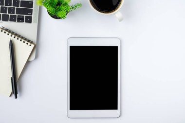 Tabletin üstündeki boş ekranın üst görüntüsü beyaz ofis masasındaki siyah ekranda defter, klavye, kahve fincanı. Çalışma alanı, ofis iş teknolojisi. Eğitim ve iş konsepti. düz yat