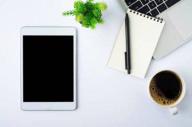 Tabletin üstündeki boş ekranın üst görüntüsü beyaz ofis masasındaki siyah ekranda defter, klavye, kahve fincanı. Çalışma alanı, ofis iş teknolojisi. Eğitim ve iş konsepti. düz yat