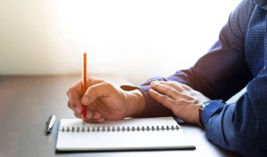Not defterine ya da mektuba kalem ya da masa başındaki günlüğe not yazarak erkek eli yakın plan. Öğrenciler için iş yeri, kopya alanı olan bir yazar. işletme çalışma ve öğrenme eğitim kavramı.