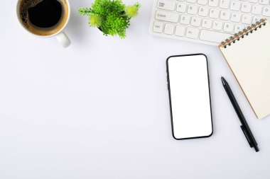 Cep telefonu boş monitörünün üst görüntüsü beyaz ofis masasında klavyeli beyaz ekran, kahve bardağı. Çalışma alanı, ofis iş teknolojisi. Eğitim ve iş konsepti. düz yat
