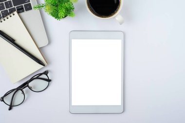 Tablet boş ekranın üst görüntüsü beyaz ofis masasında dizüstü bilgisayarlı, defterli beyaz ekran. Çalışma alanı, ofis iş teknolojisi. Eğitim ve iş konsepti. düz yat