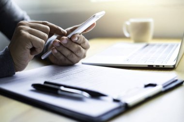 Cep telefonu kullanan bir adam internet teknolojisinde evrak işleriyle iletişim kurar. Ofis masasında dizüstü bilgisayar olur. İş yeri, profesyonel olarak yeni iş projesi fikri üzerinde çalışıyorum..