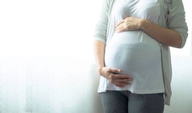 Ayakta duran, dokunan ya da elleriyle karnını okşayan bir kadının görüntüsü. Annelik, hamilelik, jinekoloji ve sağlık konsepti.