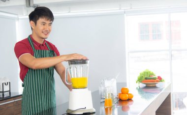 Akıllı ve yakışıklı Asyalı adam, tavan arası mutfağında sağlıklı yemek ve taze organik portakal suyu hazırlıyor..